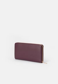 Portofel din piele mauve cu o textură netedă, formă rectangulară și detalii cu fermoar auriu pe margine. Design compact pentru stocare.