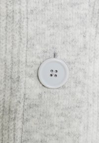 Tejido de punto gris y blanco con un gran botón gris claro de cuatro agujeros, situado de manera central en la superficie texturizada.