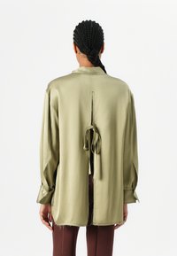 Olivengrøn satin skjorte med en afslappet pasform, rygbinding og sideslids. Har lange ærmer og en pæn krave.