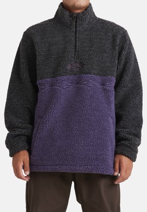 Fleece pullover with a quarter-zip design, featuring a black top and purple bottom section. Textured fabric with a geometric pattern above the purple.