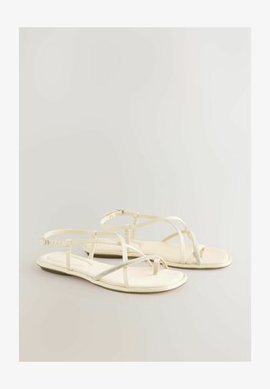 Baltos plokščios basutės su plonomis dirželiais ir mažo deimanto akcentu per pirštą. Minkštas, tekstūruotas padas ir reguliuojamas kulkšnies dirželis.