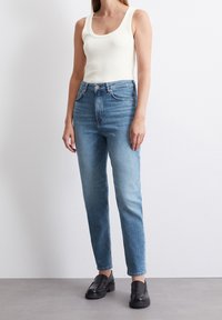 Top blanco de canalé con escote ancho, combinado con unos vaqueros de tiro alto en azul claro y mocasines negros; textura suave y silueta ajustada.