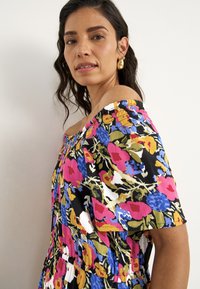 Blommig off-shoulder klänning med svart bakgrund, prydd med flerfärgade blommor i rosa, blått och grönt. Strukturerad tyg och elastisk halsringning.
