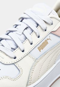 Białe skórzane sneakersy z jasnoniebieskimi akcentami, teksturowanymi panelami bocznymi i złotym logo "PUMA". Klasyczny system sznurowania z płaskimi sznurówkami.