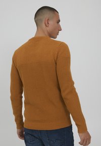 Sennepsfarget strikket genser med teksturert mønster i den øvre delen og ribbestrikkede detaljer ved ermer og underkant, tettsittende stil.