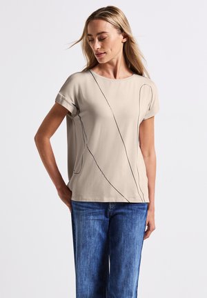 Beige korte mouw top met zwarte lijnpatronen en een losse pasvorm, gecombineerd met blauwe spijkerbroek. Gladde stof en casual ontwerp.
