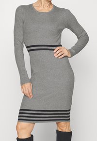 Graues, geripptes Kleid mit langen Ärmeln, das eine taillierte Silhouette hat und einen schwarzen Streifenakzent an der Taille und dem Saum aufweist. Texturiert.