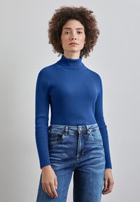 Ribbade blå turtlenecktröja gjord av stickad tyg, med figurnära långärmar. Kombinerad med högmidjade blå jeans.
