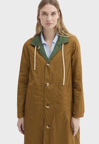 Imperméable marron mi-longueur avec un col vert, deux poches avant, boutons et cordons de serrage. Matière légère avec une texture douce.