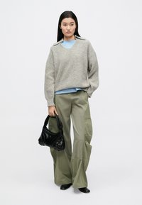 Hall hallatud üle suurusega kampsun v-kaelusega, kantud kergelt sinise särgi peal. Oliivrohelised laia säärega püksid, käes must tekstuuriga käekott.