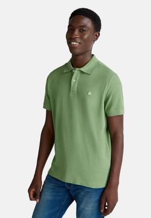 Groene poloshirt van katoen, met een klassieke kraag en een knoopsluiting met twee knopen, voorzien van een klein logo op de linkerborst. Draagt met een blauwe spijkerbroek.