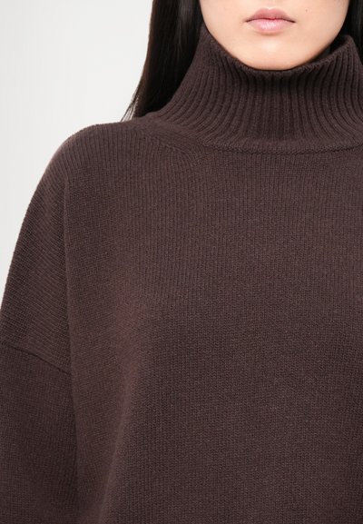 Pull à col roulé en tricot marron avec une texture côtelée, un large décolleté et une coupe ample. Le col haut apporte chaleur et style.
