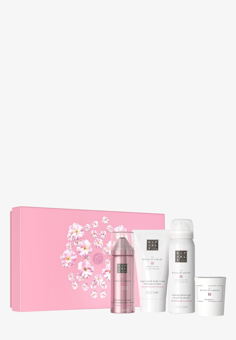 Boîte cadeau rose avec un motif floral, contenant quatre produits de soin : lotion mousse, crème pour le corps, gel douche et une bougie.