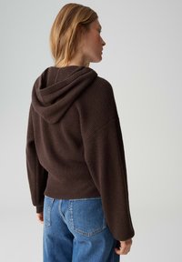 Sweat à capuche marron côtelé avec une capuche spacieuse et une coupe décontractée, associé à un jean bleu clair, affichant une apparence texturée et confortable.