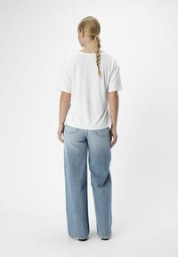 Camiseta blanca de manga corta con un corte relajado, combinada con jeans de pierna ancha en azul claro. Textura suave con detalles de costura mínimos.