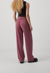 Pantalon ample taille haute en tissu bordeaux discret avec une texture subtile. Dispose d'une taille élastique et de jambes larges.