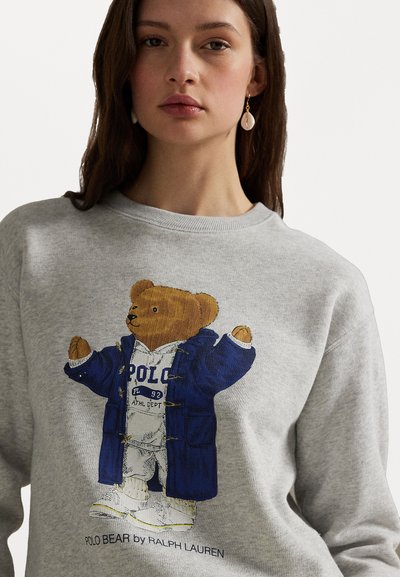 Grauer Sweatshirt mit einer Bärenillustration in einem blauen Mantel und einem weißen Outfit, mit "POLO"-Text und Details auf der Brust.