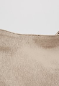 Gros plan sur un cuir beige texturé avec trois petites marques de couture verticales près du bord supérieur.