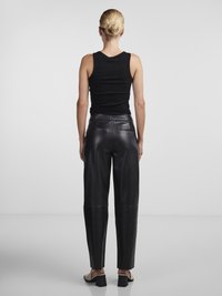 Zwart geribbelde tanktop gecombineerd met hoge zwarte leren broeken. De broeken hebben een gladde afwerking en een taps toelopend ontwerp, gedragen met open schoenen.