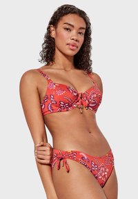 Conjunto de bikini rojo con un patrón floral, tejido suave, tirantes ajustables y detalles de lazo en la parte inferior. Incluye acentos de herrajes dorados.