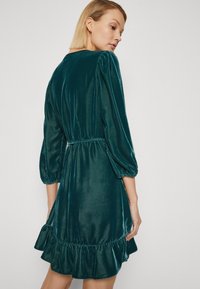 Teal sametkleit, millel on kolmveerand pikad puffvarrukad, kokku kogutud vöökohus ja volditud alläär. Sile tekstuur koos peene läike ja voogava stiiliga.