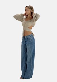 Blusa beige con maniche a sbuffo, fronte arricciato e dettagli con ritagli, abbinata a jeans a gamba larga di un azzurro chiaro a vita alta.