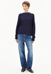 Marineblauwe pullover met een brede halslijn, gecombineerd met lichtblauwe high-waisted jeans met een rechte pijp en subtiele contrasterende stiksels.