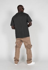 Camiseta de algodón gris oscuro de manga corta, combinada con pantalones cargo beige que tienen múltiples bolsillos, y zapatillas blancas.