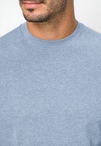 Himmelblaues Rundhals-Pullover, aus weichem Stoff gefertigt. Hat eine glatte Textur und einen gerippten Halsausschnitt. Einfaches, unverziertes Design.