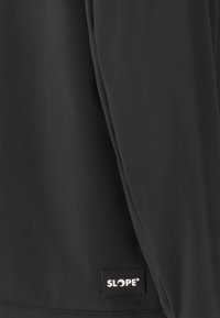 Sort langærmet top med en glat tekstur, der har et lille hvidt "SLOPE" logo-patch på den nederste side. Enkel design, tætsiddende form.