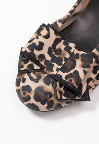 Płaskie buty w panterkę z czarną gumową podeszwą. Posiadają dużą kokardę z przodu, wykonaną z miękkiego materiału, z teksturowanymi akcentami.