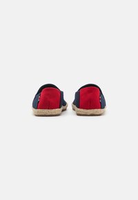 Laivastonsinisiä ja punaisia espadrille-luistokenkiä, joissa on punottu juuttipohja ja pehmeä kangas. Takakuvassa näkyy erivärisiä paneeleita.