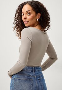 Beige Langarmoberteil mit tailliertem Schnitt, glatter Textur und rundem Ausschnitt, kombiniert mit hochgeschnittenen blauen Denim-Jeans.