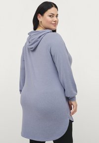 Lichtpaarse, lange mouwen tuniek met capuchon, met een ronde onderkant en zijsplitten voor een gemakkelijke beweging. Zachte, rekbare stof.