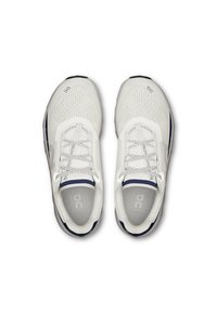 Baskets blanches de sport avec une tige en mesh respirant, un col rembourré et des accents réfléchissants. Présente une semelle texturée et des lacets plats.