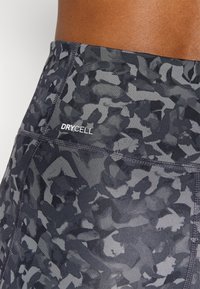 Svarta och grå mönstrade leggings gjorda av fukttransporterande tyg med en slät yta. Har "DRYCELL"-logotyp och sömnadsdetaljer.