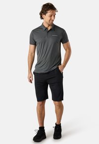 Grå polo skjorta med krage och korta ärmar, kombinerad med svarta shorts. Materialet verkar vara lätt och fuktavledande.