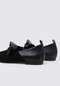 Bailarinas negras feitas de couro liso e camurça, com laços de tecido oversized na parte da frente e um design de ponta redonda. Solas de borracha.