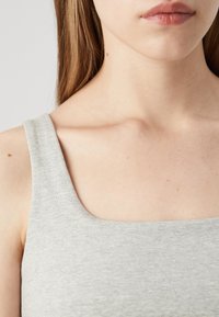 Haut sans manches gris à encolure carrée, fabriqué en tissu doux et texturé. Présente des bords lisses et une coupe ajustée.