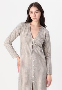 Dlhá šedá nočná košeľa s výstrihom do V, dlhými rukávmi a predným zapínaním na gombíky. Má textúrovaný vzor malých dierok po celom povrchu.