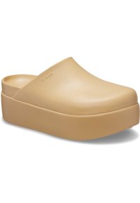 Sabots beige clair avec une tige lisse en synthétique et une semelle épaisse. Le design présente un dos ouvert et rond, avec un branding minimal.