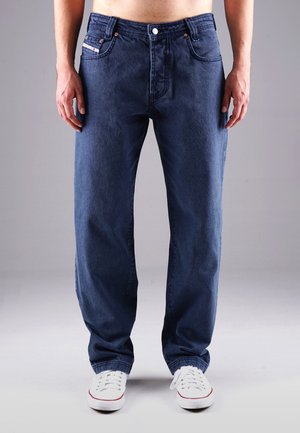 Dunkelblaue Jeans aus Denim mit geradem Schnitt, ausgestattet mit vorderen Taschen, einem Knopfverschluss und weißen Sneakers mit roten Akzenten.