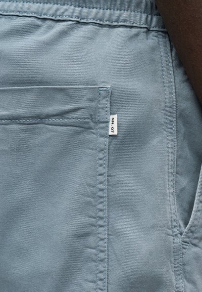 Gros plan sur la poche d'un pantalon en denim bleu clair avec des coutures visibles et une petite étiquette blanche sur le côté portant l'inscription "NN.07".