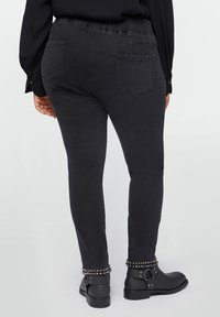 Pantalones de mezclilla negros con una cinturilla elástica, bolsillos traseros y acentos de tachuelas en el tobillo. Llevados con botas de tobillo.