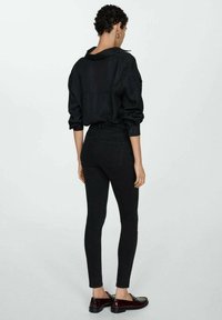 Mustapohja, jossa on kaulus, yhdistettynä korkeavyötäröisiin mustiin slim jeans -housuihin ja viininpunaisiin tasapohjaisiin kengiin. Sujuva rakenne, minimaalinen yksityiskohtaus.