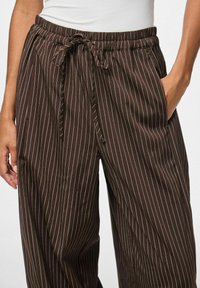 Rudos dryžuotos kelnės su elastinga juosmens juosta ir raišteliu, su šoninėmis kišenėmis ir laisvu kirpimu.