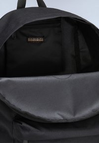 Svart ryggsäck med en texturerad yta och en zip-försedda ficka inuti. Har en rund klaffstängning och en tyglogotagg.