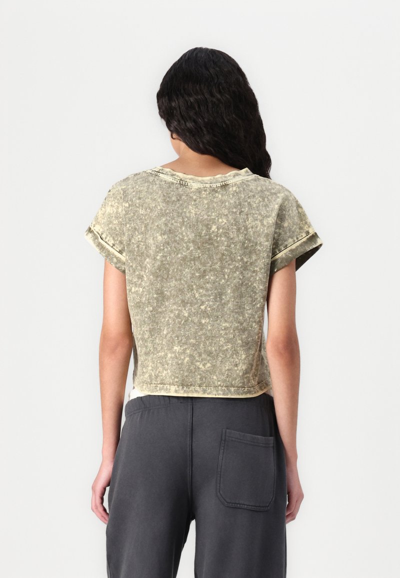 Gekürztes, olivgrünes T-Shirt mit strukturiertem Finish, kurzen Ärmeln und rundem Ausschnitt. Der Saum ist leicht geschwungen und mit sichtbaren Nähten versehen.