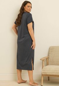 Abito grigio a lunghezza ginocchio con maniche corte, realizzato in tessuto morbido, presentante spacco laterale e una vestibilità comoda, indossato da una persona che sta in piedi a piedi nudi.