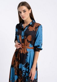 Długa sukienka z kołnierzykiem, ozdobiona niebieskim i brązowym wzorem kwiatowym na czarnym tle; zebrana w talii brązowym paskiem. Gładki materiał.